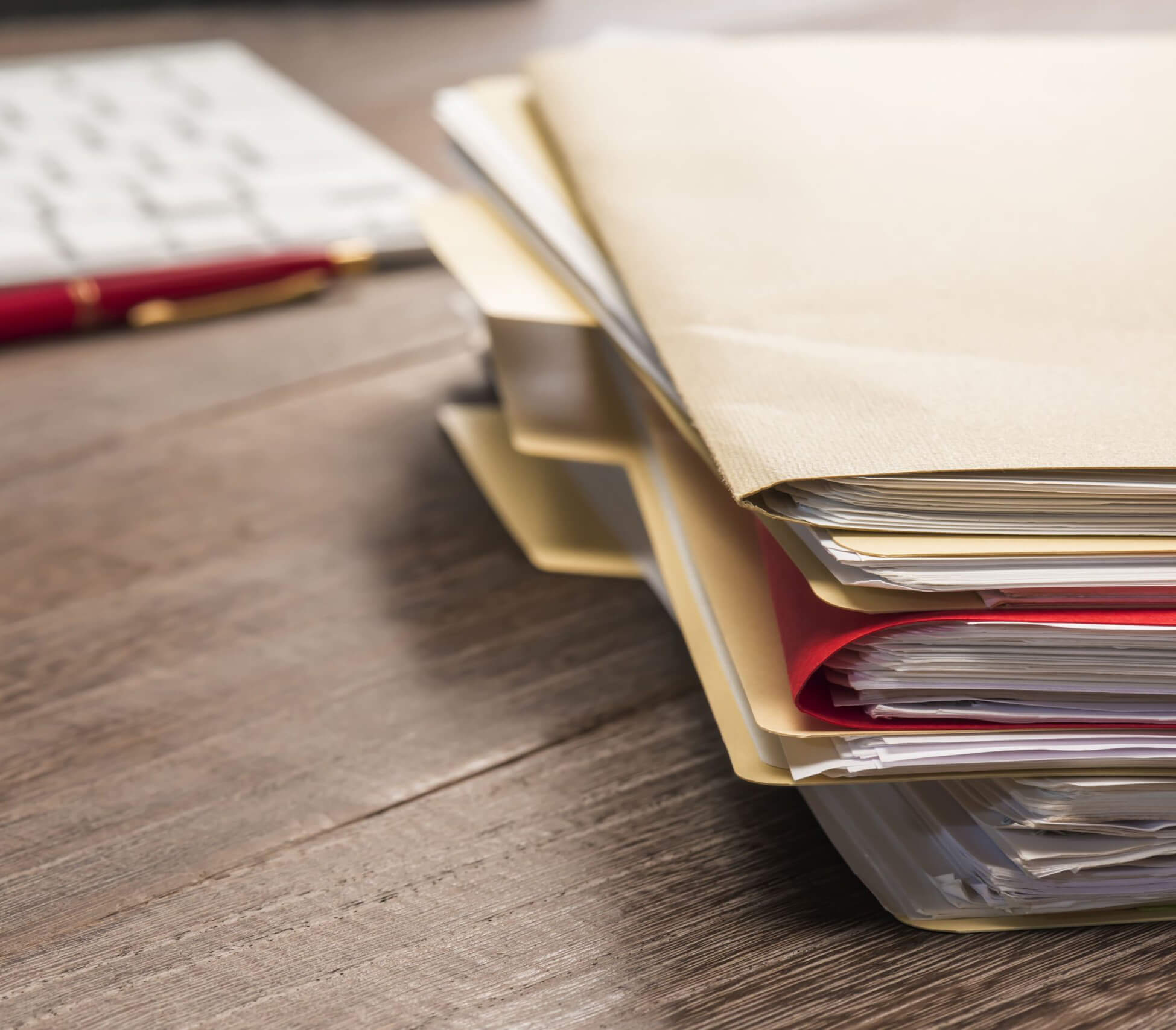 Image of a stack of paperwork in files on a desk next to a pen and a keyboard